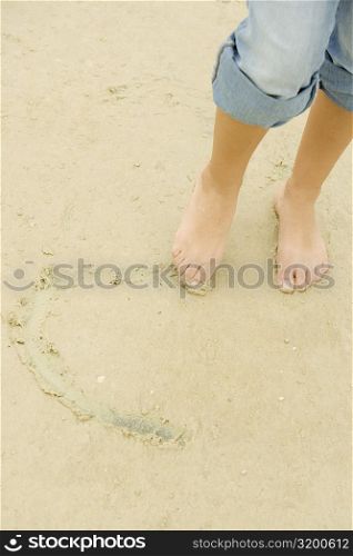 Low section view of a woman drawing in sand with her toe
