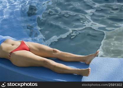 Low section view of a woman lying on the ledge of a swimming pool
