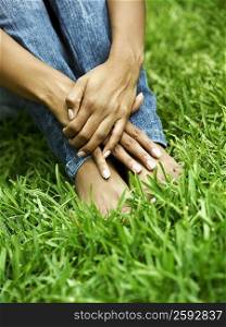 Low section view of a woman sitting on the grass with hugging her knees