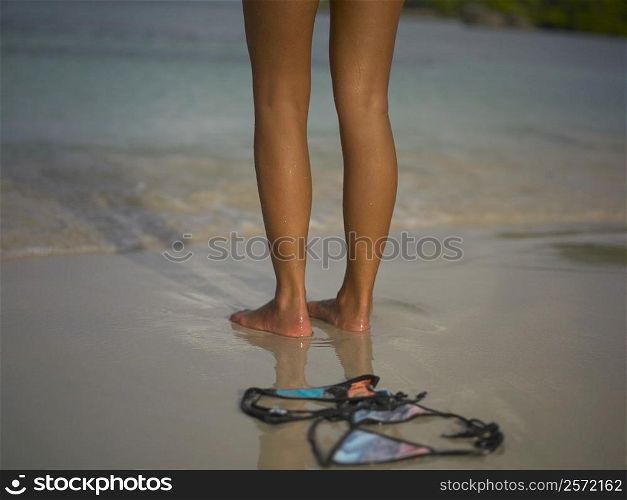 Low section view of a woman standing on the beach near a bikini