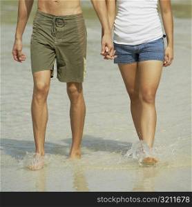 Low section view of a young couple holding hands and walking on the beach