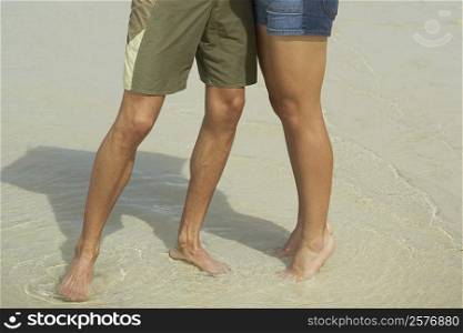 Low section view of a young man and a teenage girl standing on the beach