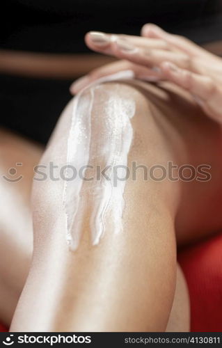 Low section view of a young woman applying moisturizer on her knee