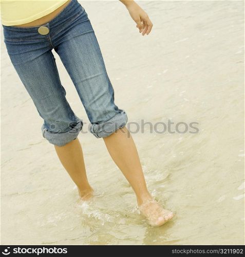 Low section view of a young woman wading in water on the beach