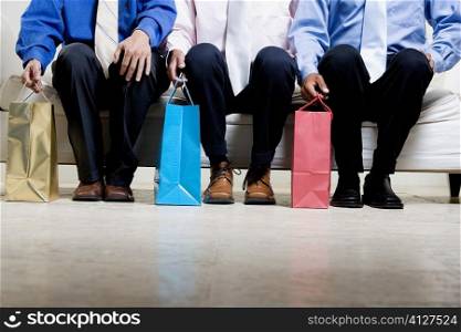 Low section view of three businessmen sitting with shopping bags