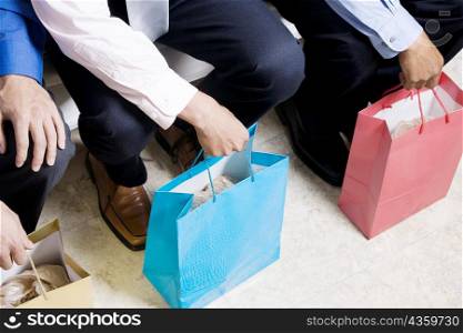 Low section view of three businessmen sitting with shopping bags