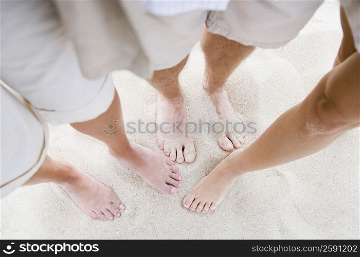 Low section view of three people standing on sand