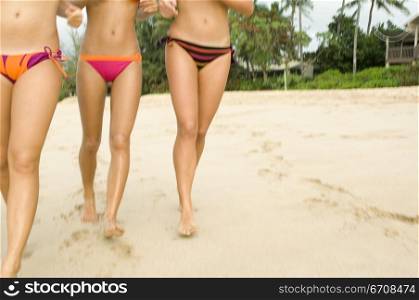 Low section view of three women walking on the beach