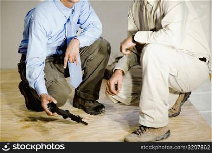Low section view of two male architects crouching on a hardwood floor