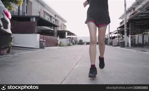 Lower angle of female running in front of house neighborhood street, get fit human vitality, relaxing exercise cool down, car parked along the side, work out during sunset, urban active lifestyle