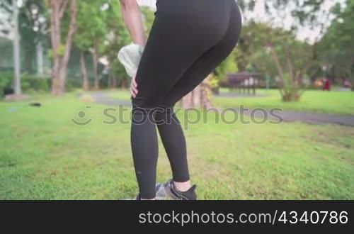 Lower body part of young woman bending knees doing warm up exercise before running inside the park, green grass field and running track on the background, doing exercise during Coronavirus pandemic