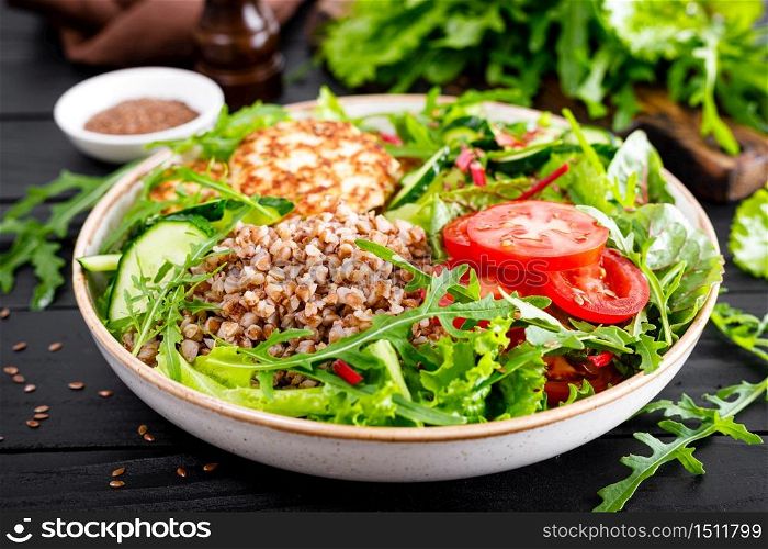 Lunch bowl with buckwheat porridge, fried chicken cutlets and fresh vegetable salad of arugula, lettuce, chard leaves, tomato, cucumber and flax seeds