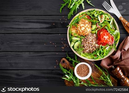 Lunch bowl with buckwheat porridge, fried chicken cutlets and fresh vegetable salad of arugula, lettuce, chard leaves, tomato, cucumber and flax seeds