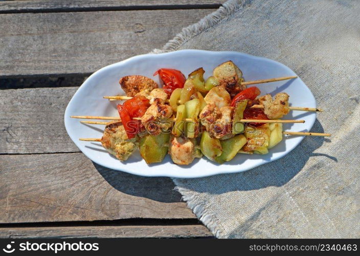 Lunch grilled chicken and vegetable skewers. White plate on a checkered green tablecloth. Lunch grilled chicken