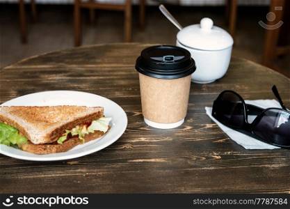 Lunch with triangle sandwich, takeaway coffee and sunglasses on dark wooden table. Lunch with triangle sandwich, takeaway coffee and sunglasses on wooden table