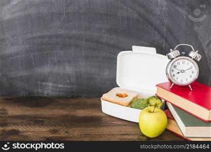 lunchbox apple near books alarm clock