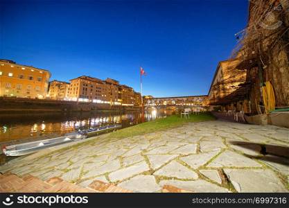 Lungarni in Florence at night with Arno River reflections and tiles on foreground.