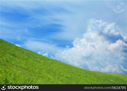Lush, green hill with blue sky and clouds.