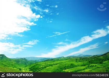 Lush, green landscape with blue sky and clouds.