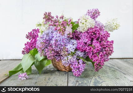 Lush multicolored bouquet of lilac flowers in a basket on an old wooden background