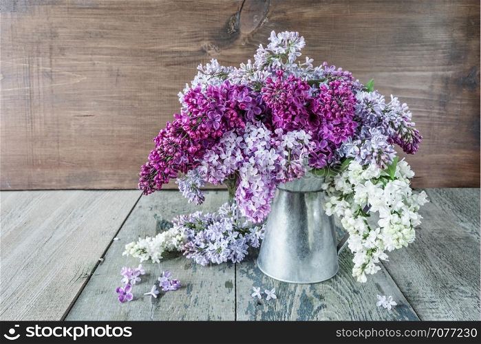 Lush wet multicolored bouquet of lilac flowers in a metal pitcher on an old wooden background