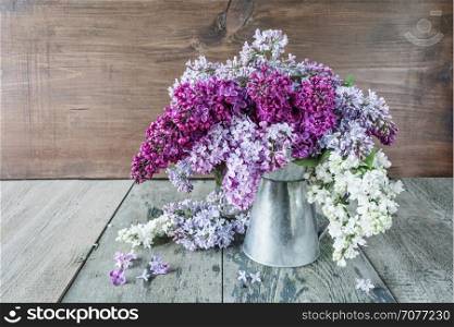 Lush wet multicolored bouquet of lilac flowers in a metal pitcher on an old wooden background