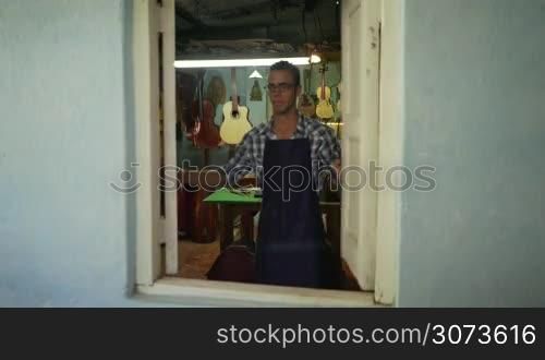 Lute maker shop and classical music instruments: young adult artisan opening his shop. He fixes an old classic guitar lacking a string. Dolly shot