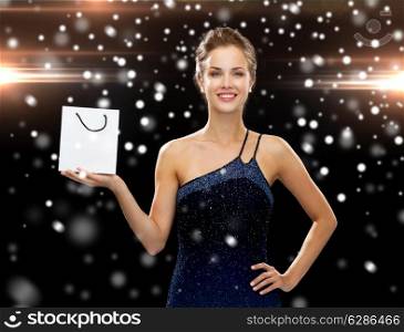 luxury, advertisement, christmas, holidays and sale concept - smiling woman with white blank shopping bag over night lights and snow background