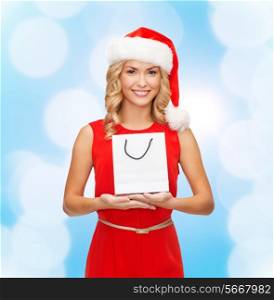 luxury, advertisement, holydays and sale concept - smiling woman in santa helper hat with white blank shopping bag over blue lights background