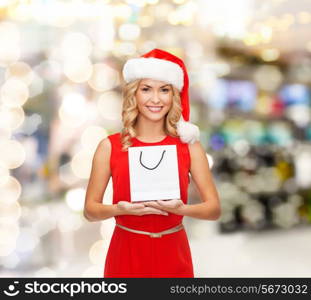 luxury, advertisement, holydays and sale concept - smiling woman in santa helper hat with white blank shopping bag over lights background