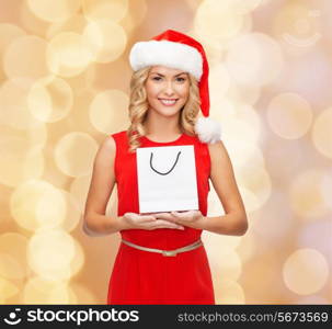 luxury, advertisement, holydays and sale concept - smiling woman in santa helper hat with white blank shopping bag over beige lights background