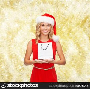 luxury, advertisement, holydays and sale concept - smiling woman in santa helper hat with white blank shopping bag over yellow lights background