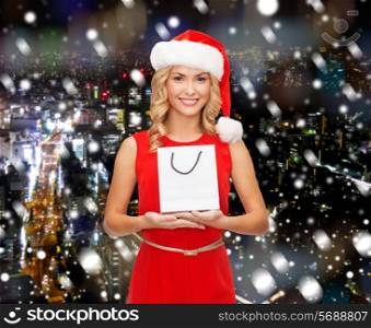 luxury, advertisement, holydays and sale concept - smiling woman in santa helper hat with white blank shopping bag over snowy night city background
