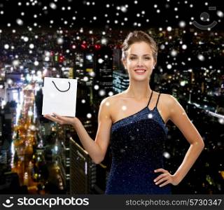 luxury, advertisement, holydays and sale concept - smiling woman with white blank shopping bag over snowy night city background