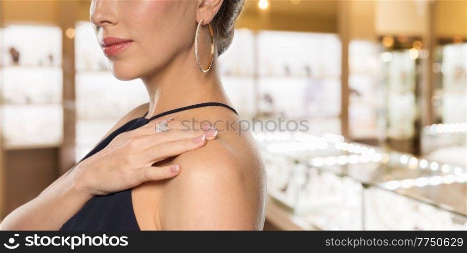 luxury and people concept - beautiful woman in black dress wearing diamond ring and earrings over jewelry store background. woman with diamond ring at jewelry store