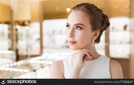 luxury and people concept - beautiful woman in evening dress wearing diamond earring over jewelry store background. woman with diamond earring at jewelry store