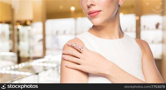 luxury and people concept - beautiful woman in evening dress wearing diamond ring and earring over jewelry store background. woman with diamond ring at jewelry store