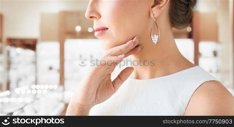 luxury and people concept - beautiful woman in evening dress wearing pearl earrings over jewelry store background. woman wearing pearl earring at jewelry store