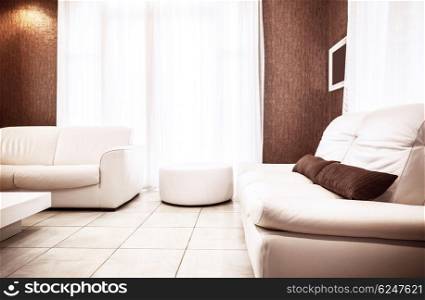 Luxury apartment interior in white&amp;brown colours, two stylish leather couch and pouf, bright sun light through big window, cozy flat concept