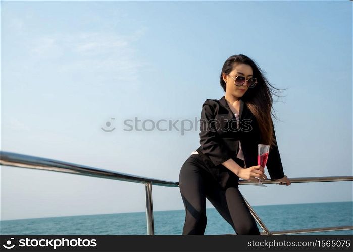 Luxury asian woman in black suit drinking champagne on the yacht.