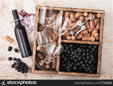 Luxury bottle of red wine and empty glasses with dark grapes with corks and opener inside vintage wooden box on wooden background .