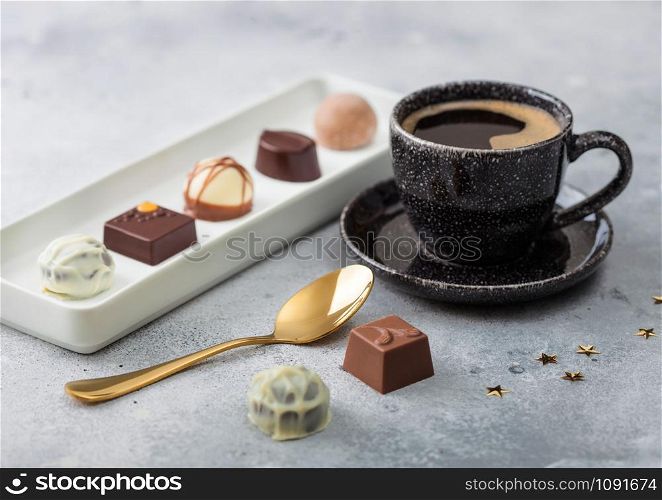 Luxury Chocolate candies in white porcelain plate with cup of black coffee and golden spoon on light background.