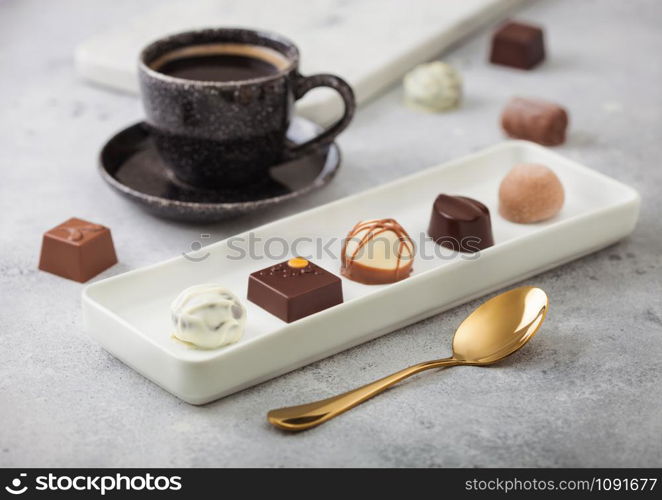 Luxury Chocolate candies in white porcelain plate with cup of black coffee and golden spoon on light background.