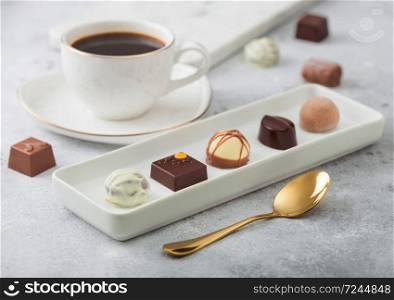 Luxury Chocolate candies in white porcelain plate with cup of black coffee and golden spoon on light background.