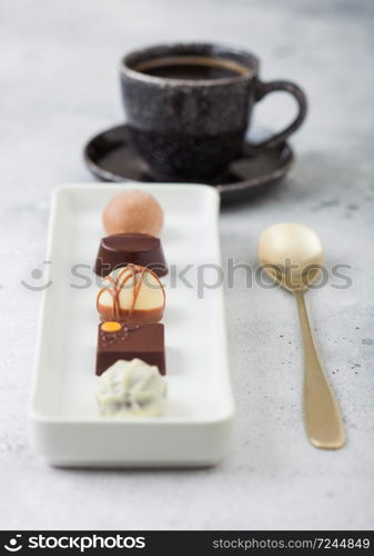 Luxury Chocolate candies in white porcelain plate with cup of black coffee and dessert spoon on light background.