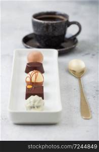 Luxury Chocolate candies in white porcelain plate with cup of black coffee and dessert spoon on light background.