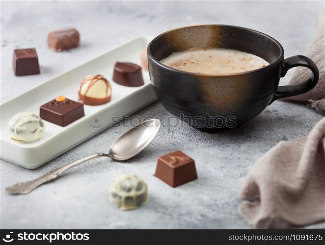 Luxury Chocolate candies in white porcelain plate with cup of cappuccino coffee and silver spoon on light background.
