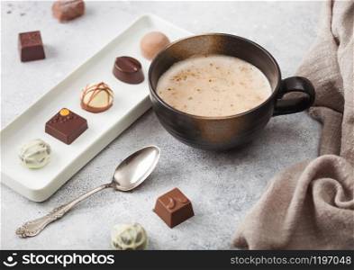 Luxury Chocolate candies in white porcelain plate with cup of cappuccino coffee and silver spoon on light background.