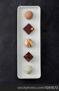 Luxury Chocolate candies selection in white porcelain plate on black background.White, dark and milk chocolate assortment. Top view