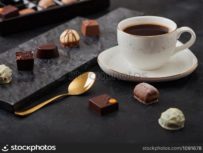 Luxury Chocolate candies selection with cup of black coffee and golden spoon on black marble board and dark background.